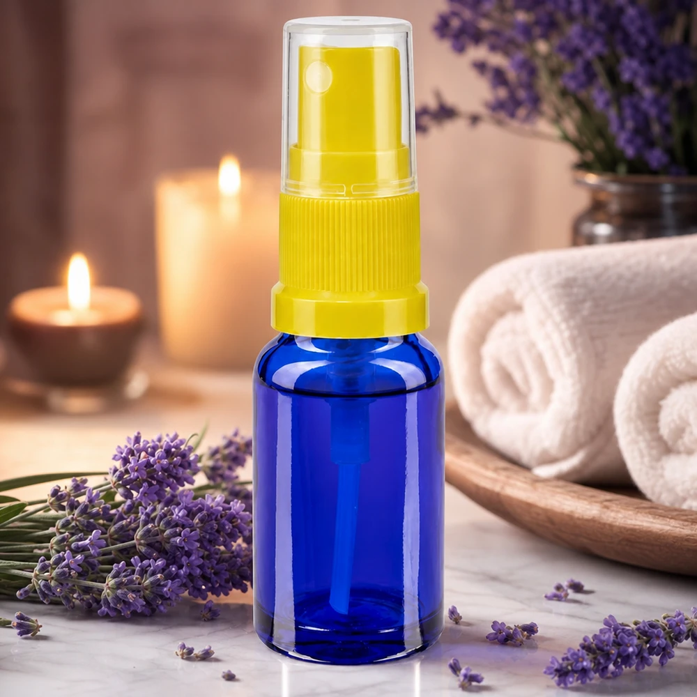 Butelka apteczna niebieska 30ml nasadka rozpylająca żółta Akcesoria do aromaterapii: niebieska butelka z atomizerem o pojemności 30 ml z żółtą nasadką obok kwiatów lawendy