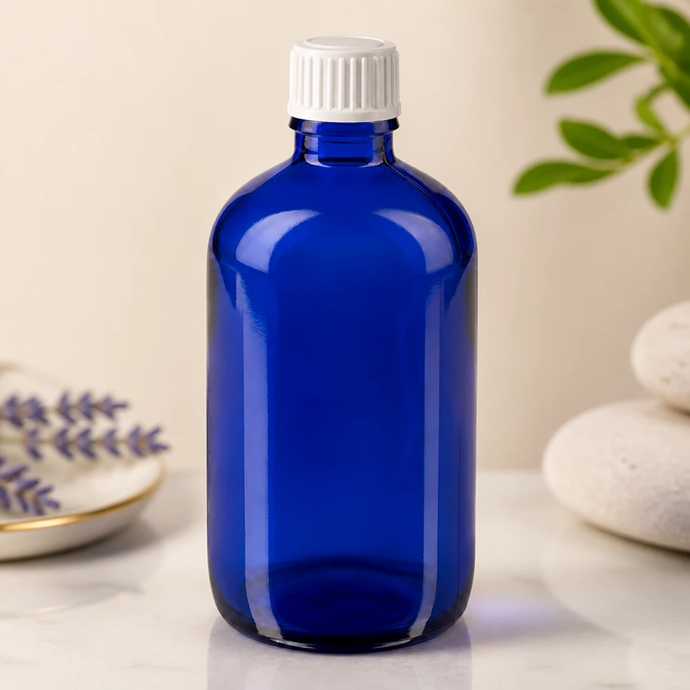 Butelka apteczna niebieska 100ml zakrętka biała szt. Niebieska szklana butelka o pojemności 100 ml z białym zamknięciem zabezpieczającym przed dziećmi, stojąca na marmurowej powierzchni obok lawendy