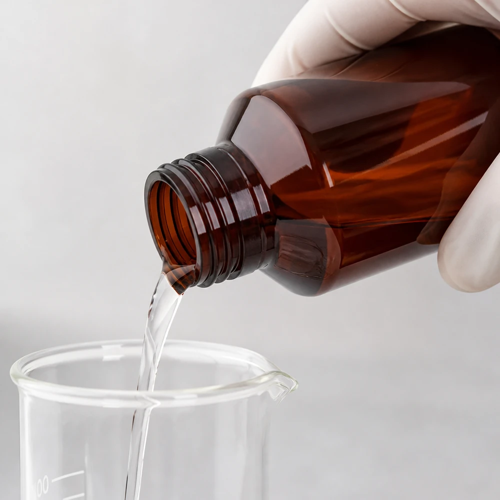 Butelka PET 100ml z zieloną nakrętką OV Przezroczysty płyn przelewa się z brązowej butelki PET o pojemności 100 ml do szklanego kubka