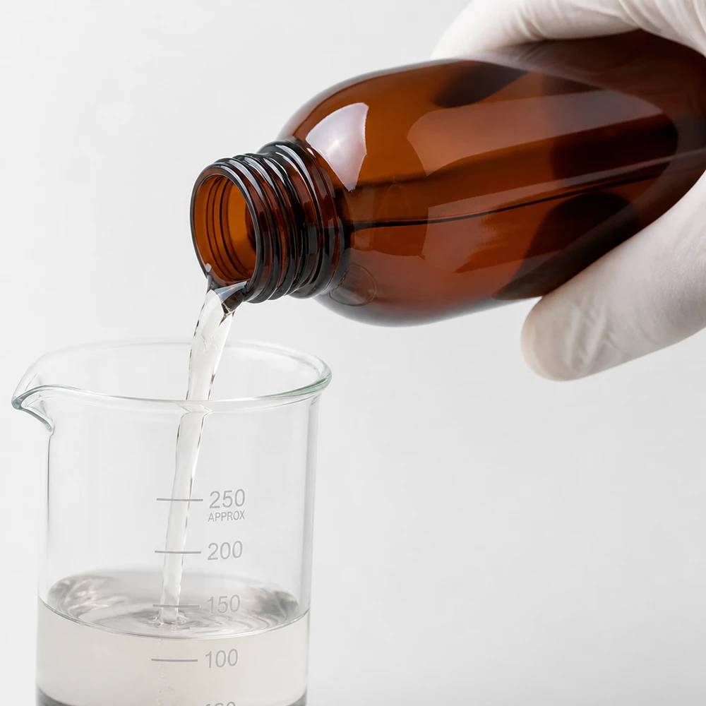 Schutzhandschuh hält bernsteinfarbene 250ml Flasche beim Dosieren in graduiertes Becherglas