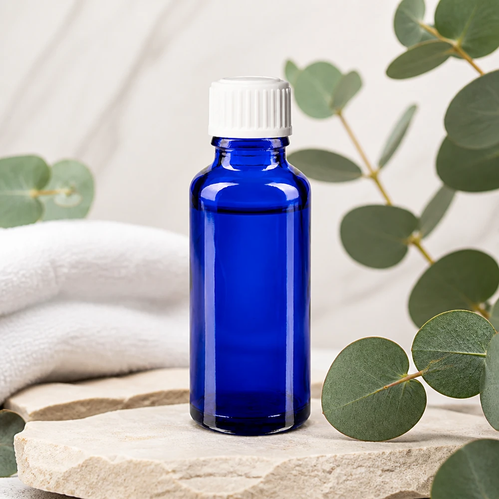 Butelka apteczna niebieska 30ml zakrętka biała szt. Kobaltowo-niebieska buteleczka apteczna o pojemności 30 ml z białym zakraplaczem, stojąca na kamieniu naturalnym z motywem eukaliptusa