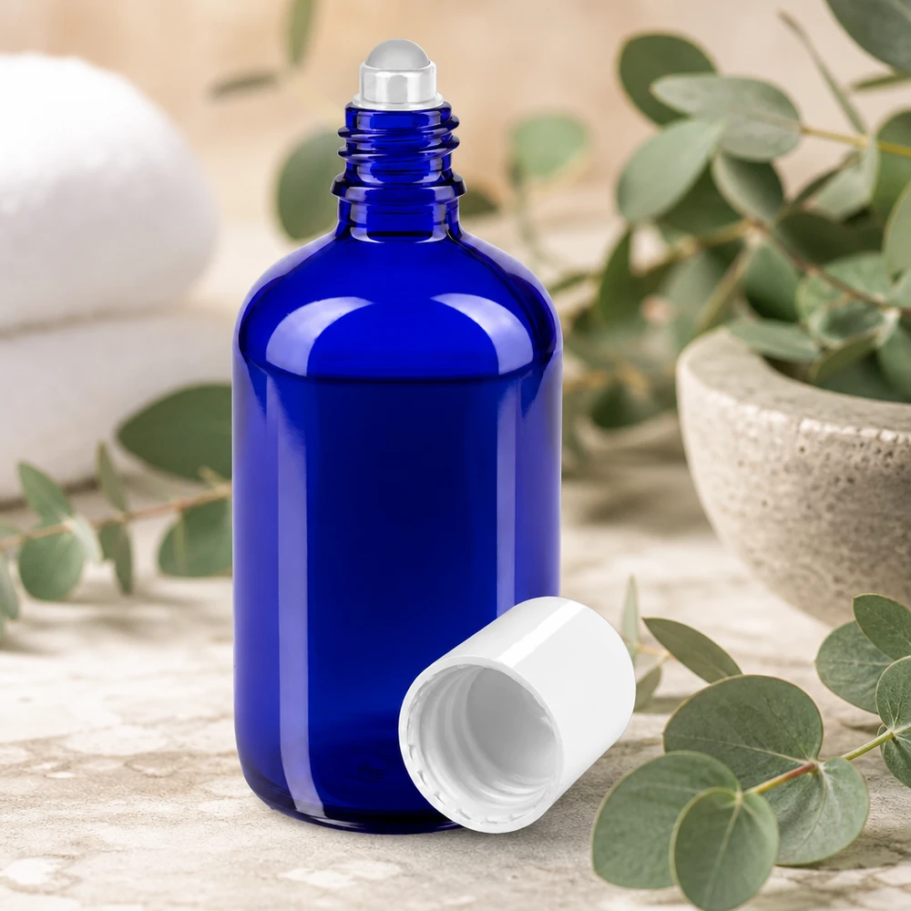 Butelka apteczna niebieska 100ml nakrętka roll-on biała Niebieska buteleczka z kulką o pojemności 100 ml, ze stalową kulką i białą nakrętką, umieszczona wśród gałązek eukaliptusa