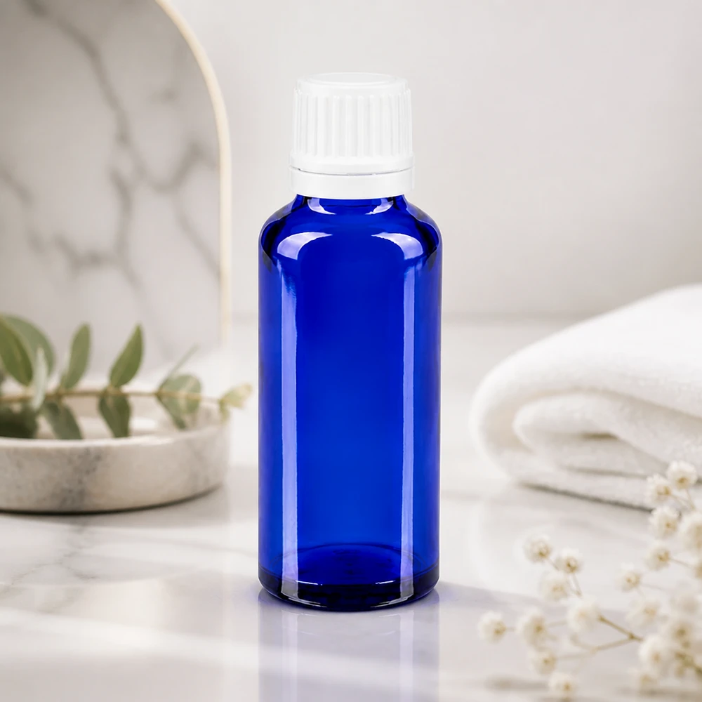 Butelka apteczna niebieska 30ml drip v. 1,2 mm biały OV Niebieska buteleczka apteczna o pojemności 30 ml z kroplomierzem 0,7 mm na białym marmurze obok złożonego ręcznika