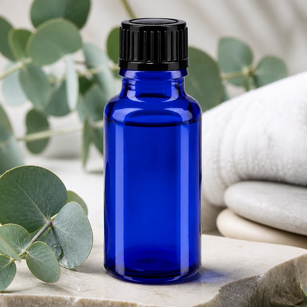 Butelka apteczna niebieska 20ml zakrętka czarna szt. Mała niebieska buteleczka apteczna o pojemności 20 ml z czarną nakrętką, ustawiona na kamieniu naturalnym z eukaliptusem