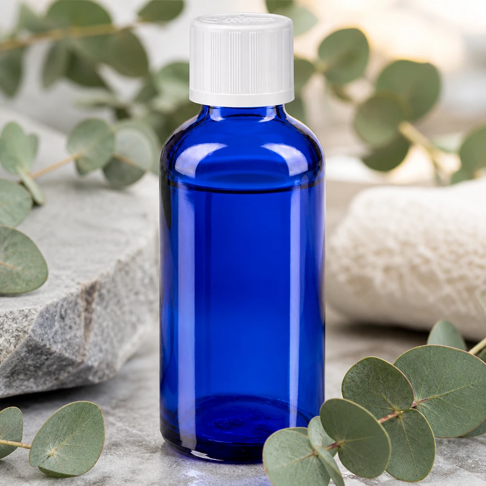 Kobaltowo-niebieska butelka aptekarska o pojemności 50 ml z białym zamknięciem KiSi, stojąca na kamieniu naturalnym wśród gałązek eukaliptusa