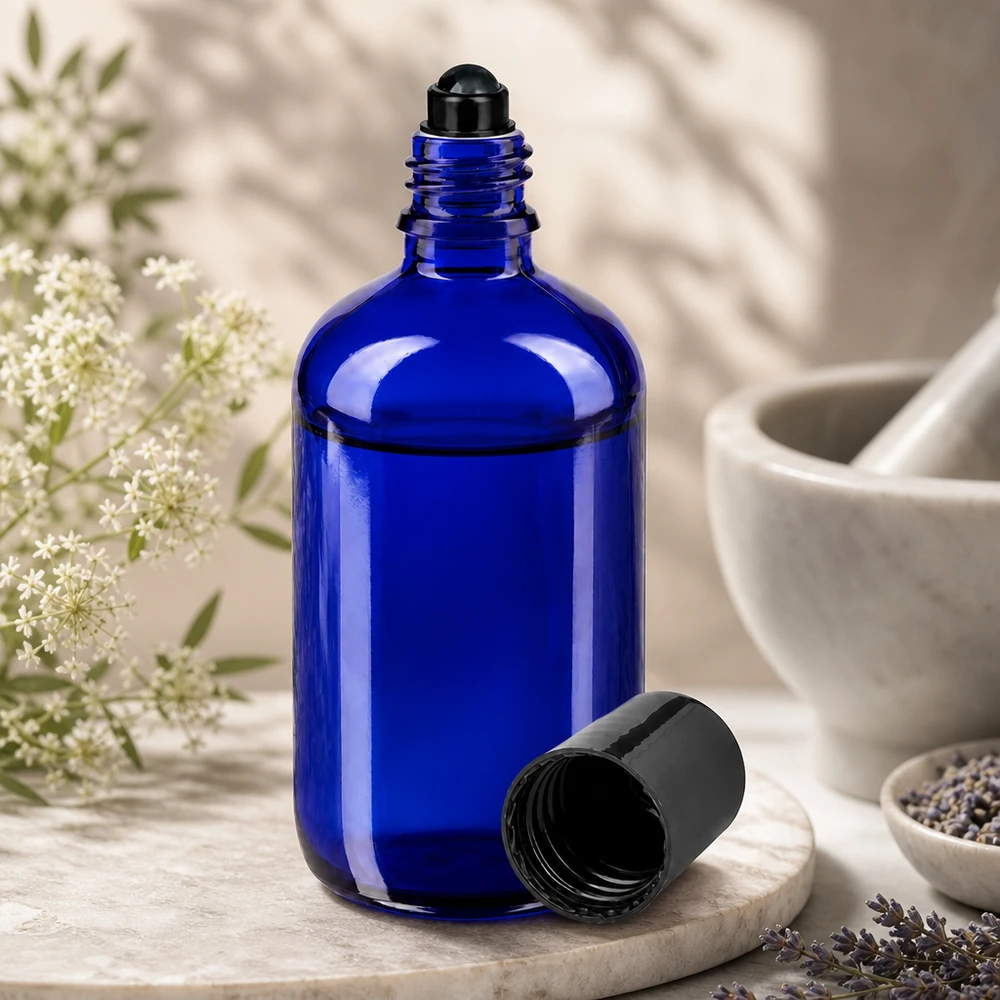 Kobaltowo-niebieska szklana butelka o pojemności 100 ml z czarną kulką, otwarta, obok kwiatów lawendy i moździerza