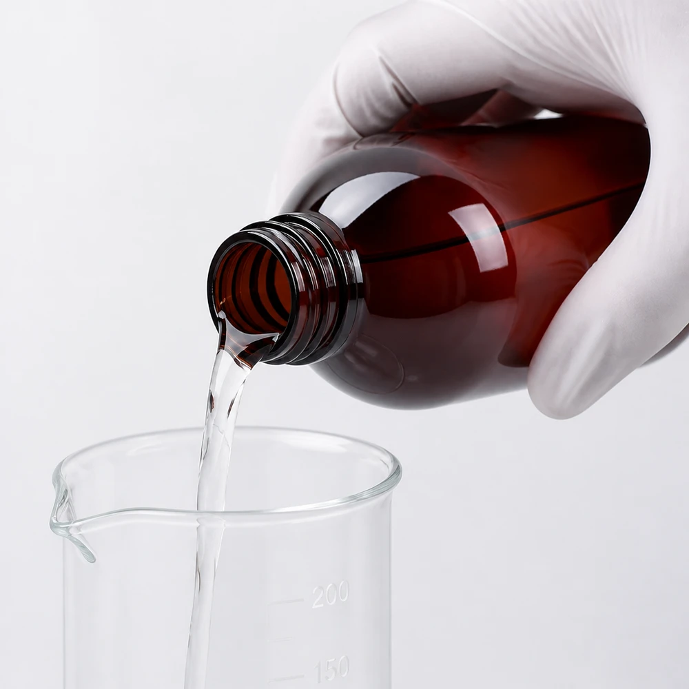 Brązową butelkę PET o pojemności 250 ml wlewa się do zlewki laboratoryjnej, mając na rękach rękawiczki ochronne
