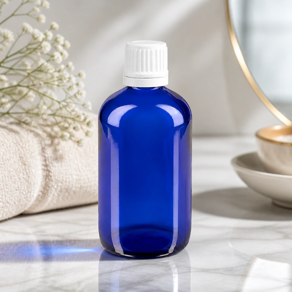 Butelka apteczna niebieska 100ml zakrętka biała OV Niebieska szklana butelka o pojemności 100 ml z białym zamknięciem typu OV, stojąca na marmurze obok ręcznika i suszonych kwiatów