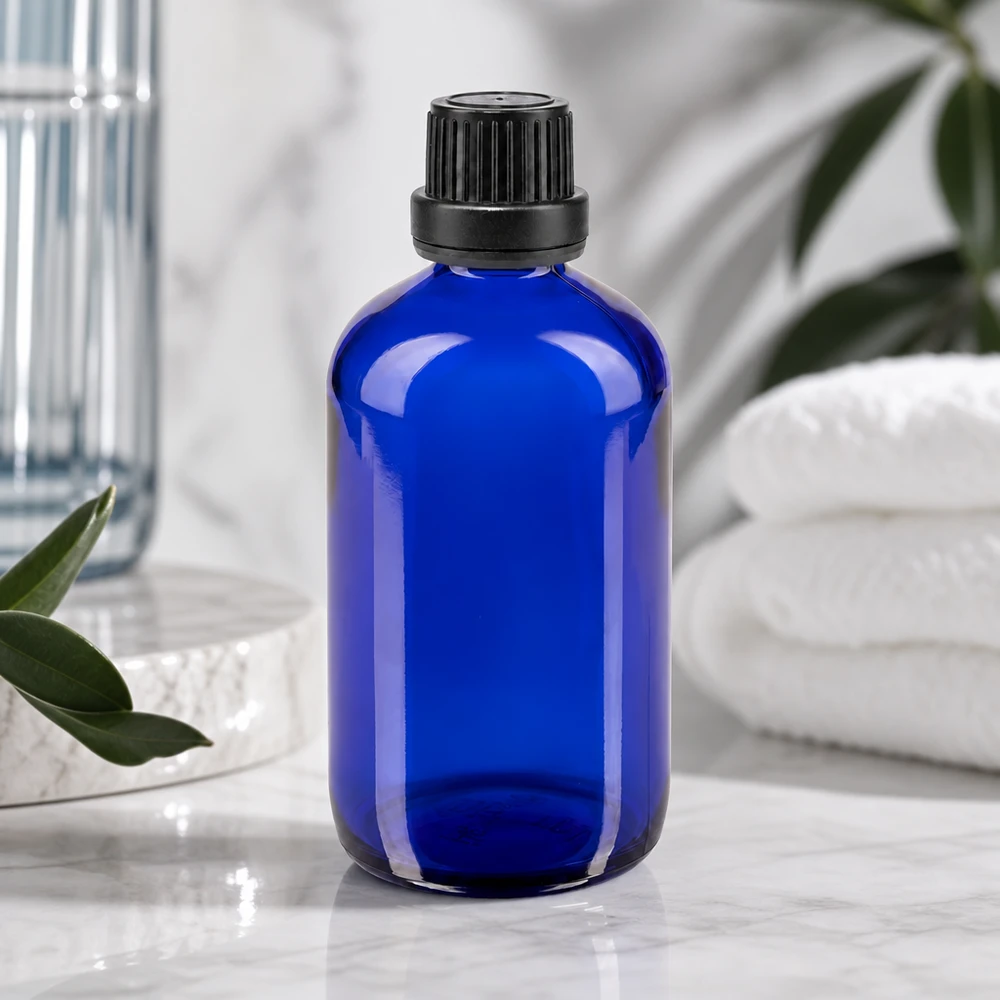 Butelka apteczna niebieska 100ml zakrętka czarna szczelna OV Niebieska szklana butelka o pojemności 100 ml z żebrowaną czarną nakrętką obok białych ręczników i zielonych roślin