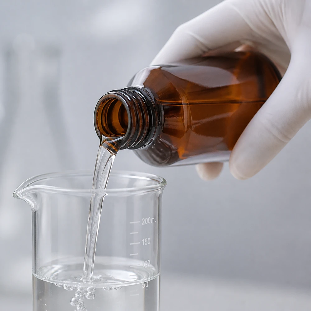 Laborant przelewa przezroczysty płyn z brązowej butelki do zlewki z podziałką do 200 ml