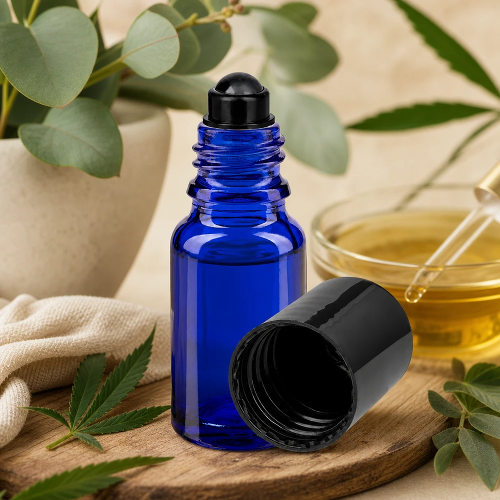 Niebieska buteleczka typu roll-on ApoGlas o pojemności 10 ml z czarną nakrętką, stojąca na drewnianej deseczce obok liścia konopi i eukaliptusa