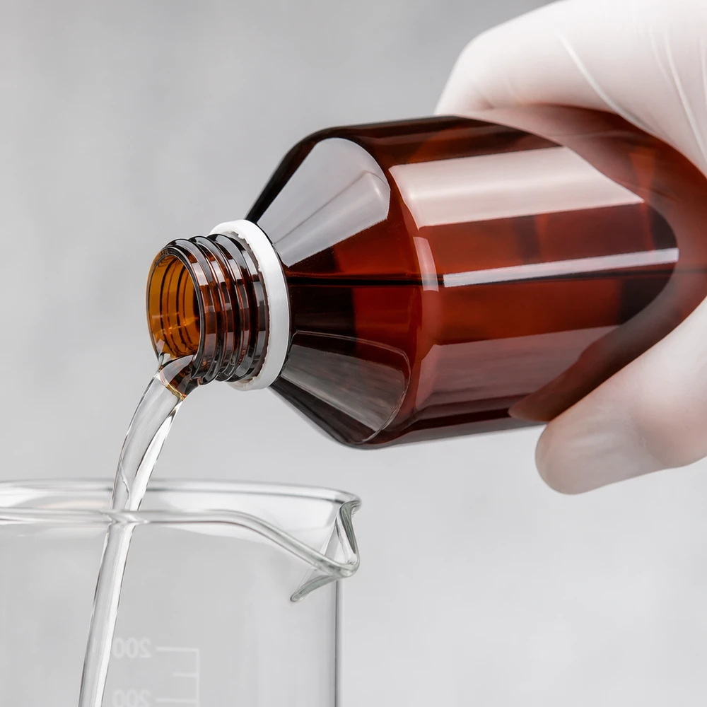 Butelka PET 500 ml z białym karbowanym OV Przezroczysty płyn przelewa się z brązowej butelki PET o pojemności 500 ml do zlewki z białym zamknięciem typu OV