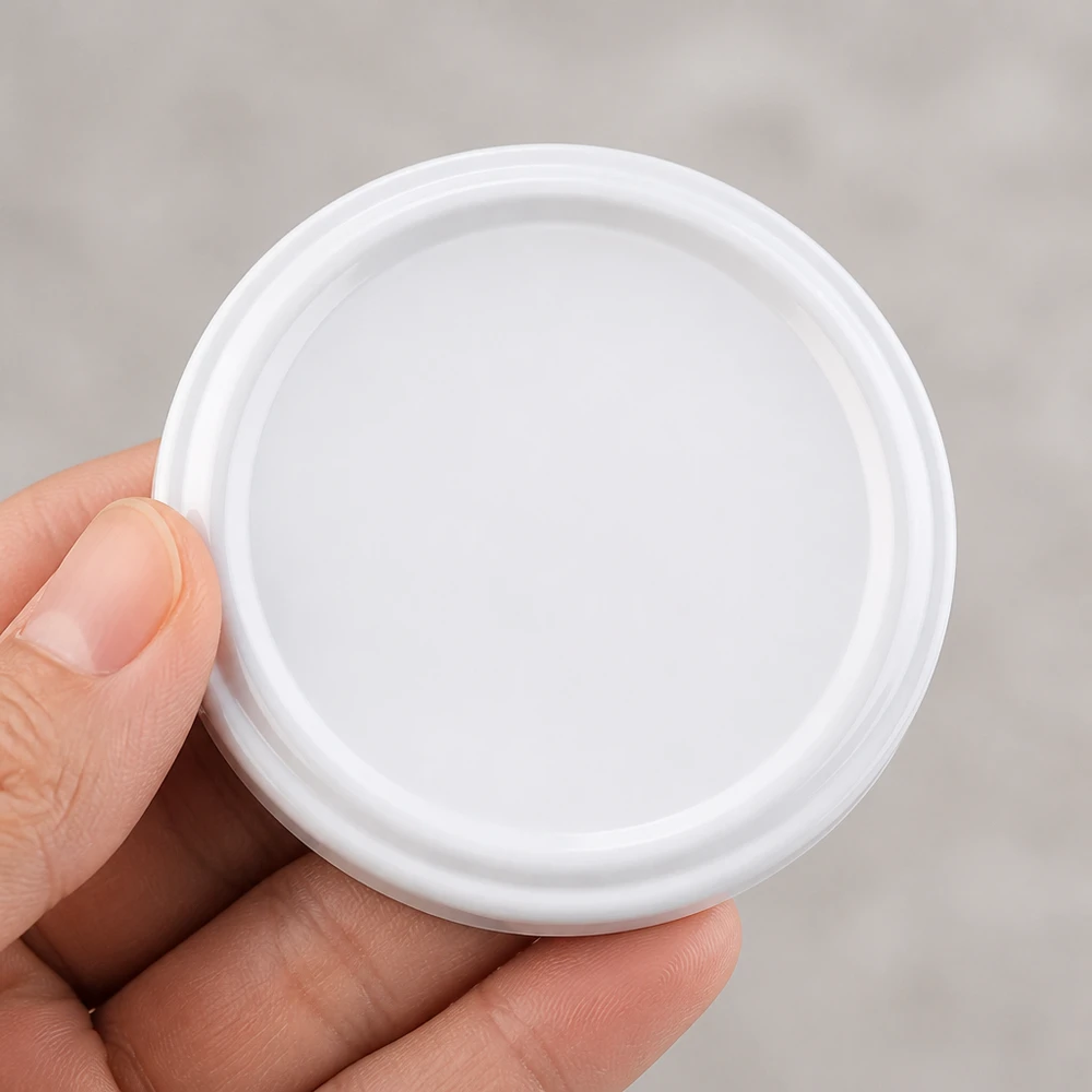 UNiTWIST TO58 biały, BioSeal, bez BPA, unitemp UNiTWIST TO58 – biała plastikowa pokrywka o średnicy 58 mm z uszczelką BioSeal w dłoni