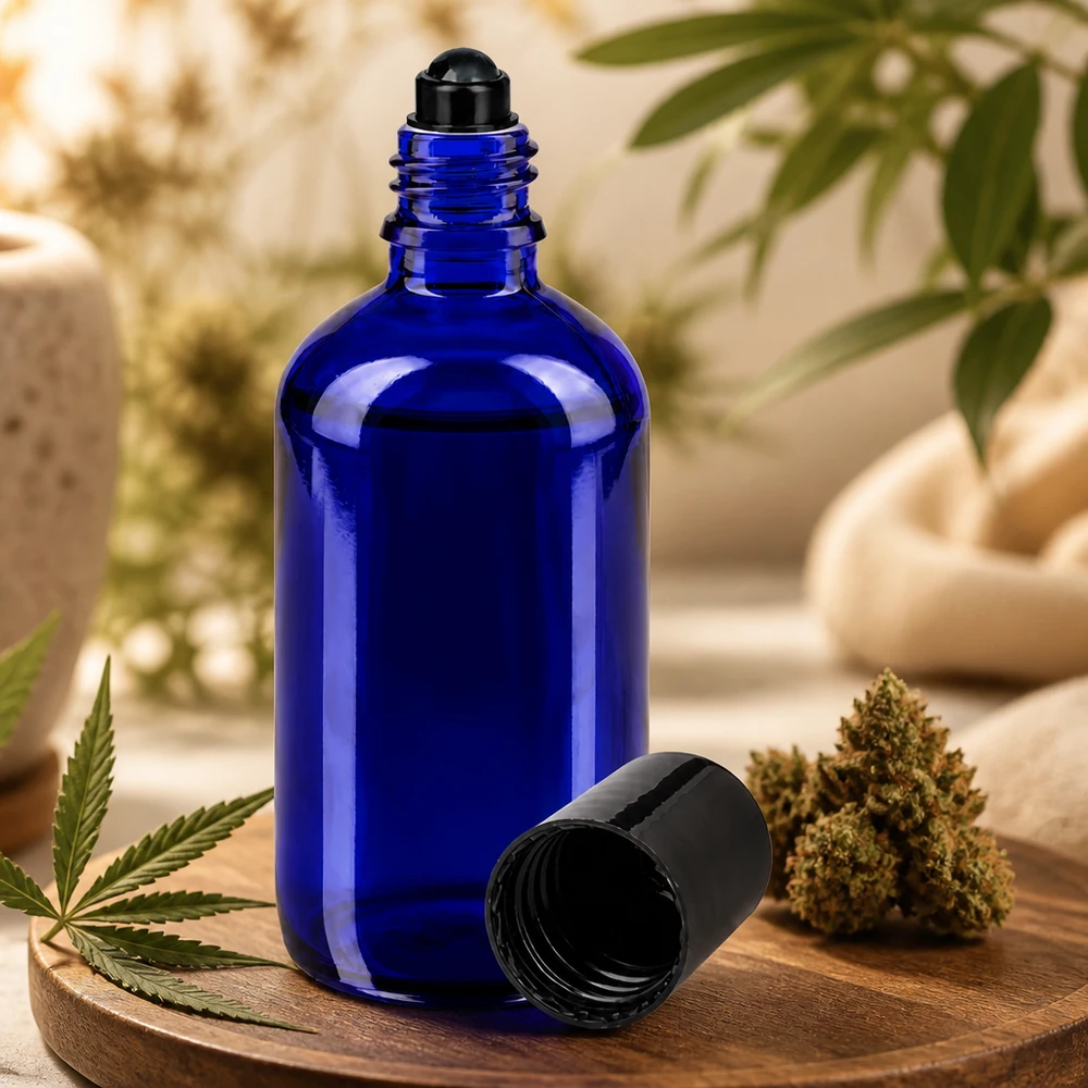 Butelka apteczna niebieska 100ml zakrętka roll-on czarna Niebieska buteleczka z kulką o pojemności 100 ml, wykonana ze szkła aptecznego, obok kwiatu konopi i liścia konopi na drewnianej deseczce