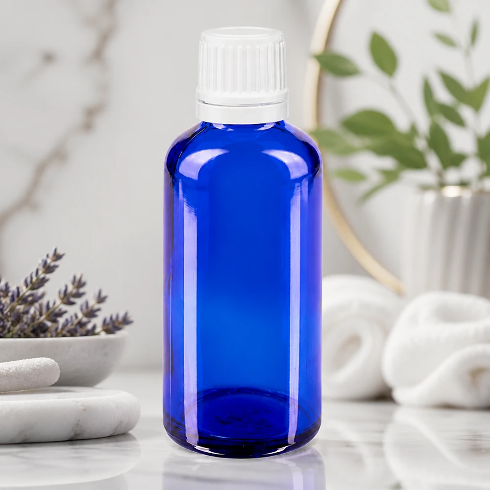 Niebieska szklana butelka o pojemności 50 ml z białą zakrętką, stojąca na marmurze obok lawendy