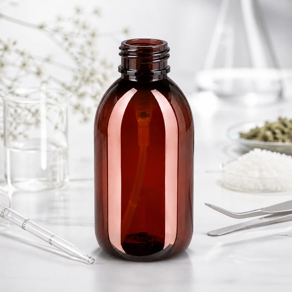 Pusta butelka PET o pojemności 250 ml w kolorze bursztynowo-brązowym, bez nakrętki, na białym blacie laboratoryjnym wraz z przyborami laboratoryjnymi