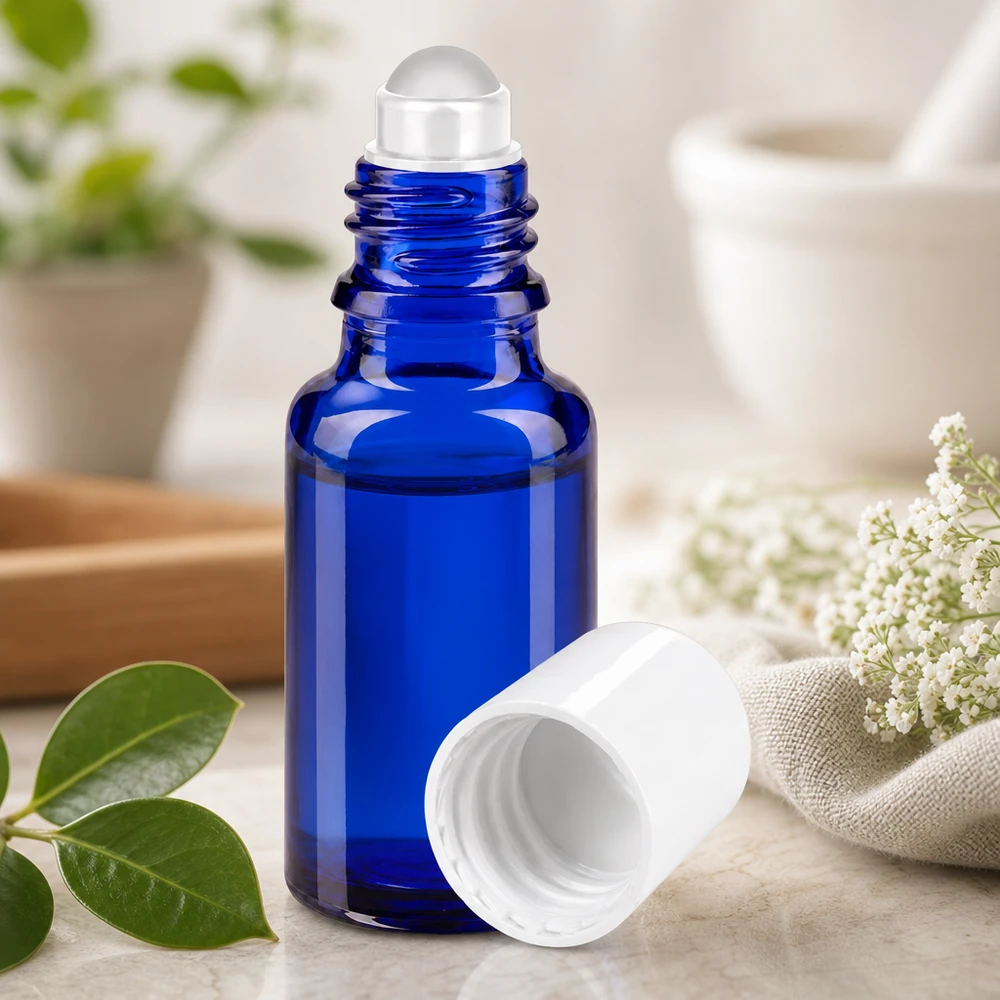 Butelka apteczna niebieska 20ml nakrętka roll-on biała Niebieska szklana buteleczka apteczna o pojemności 20 ml z przezroczystą kulką rolkową obok białych kwiatów i zielonych liści