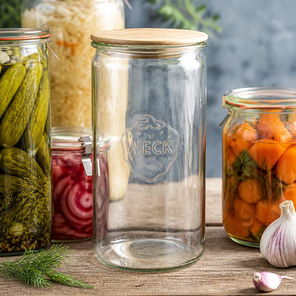 Słoik cylindryczny WECK RR100 o pojemności 1590 ml z drewnianą pokrywką WECK Zylinderglas 1590ml RR100 mit Holzdeckel zwischen Einmachgläsern mit Gurken Karotten und Sauerkraut auf Holztisch
