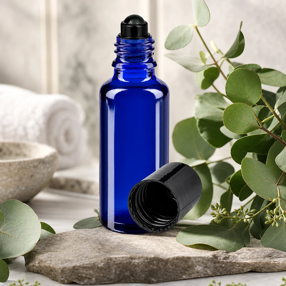 Szklana buteleczka o pojemności 30 ml w kolorze kobaltowym z czarną nakładką typu roll-on, umieszczona na kamieniu naturalnym wśród gałązek eukaliptusa