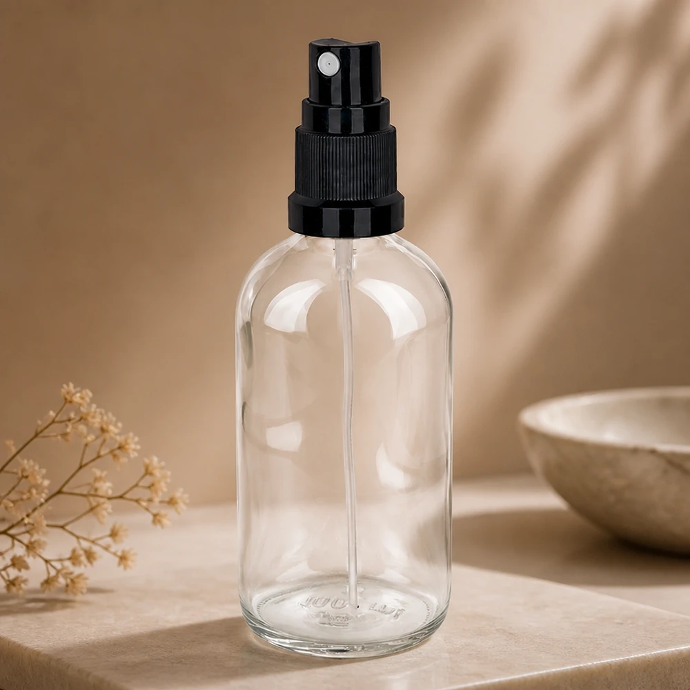 100 ml butelka ze spryskiwaczem czarna STD ClearLine UT18/100 Przezroczysta szklana butelka z atomizerem o pojemności 100 ml z czarną głowicą rozpylającą o drobnej mgiełce, umieszczona na jasnej marmurowej podstawie