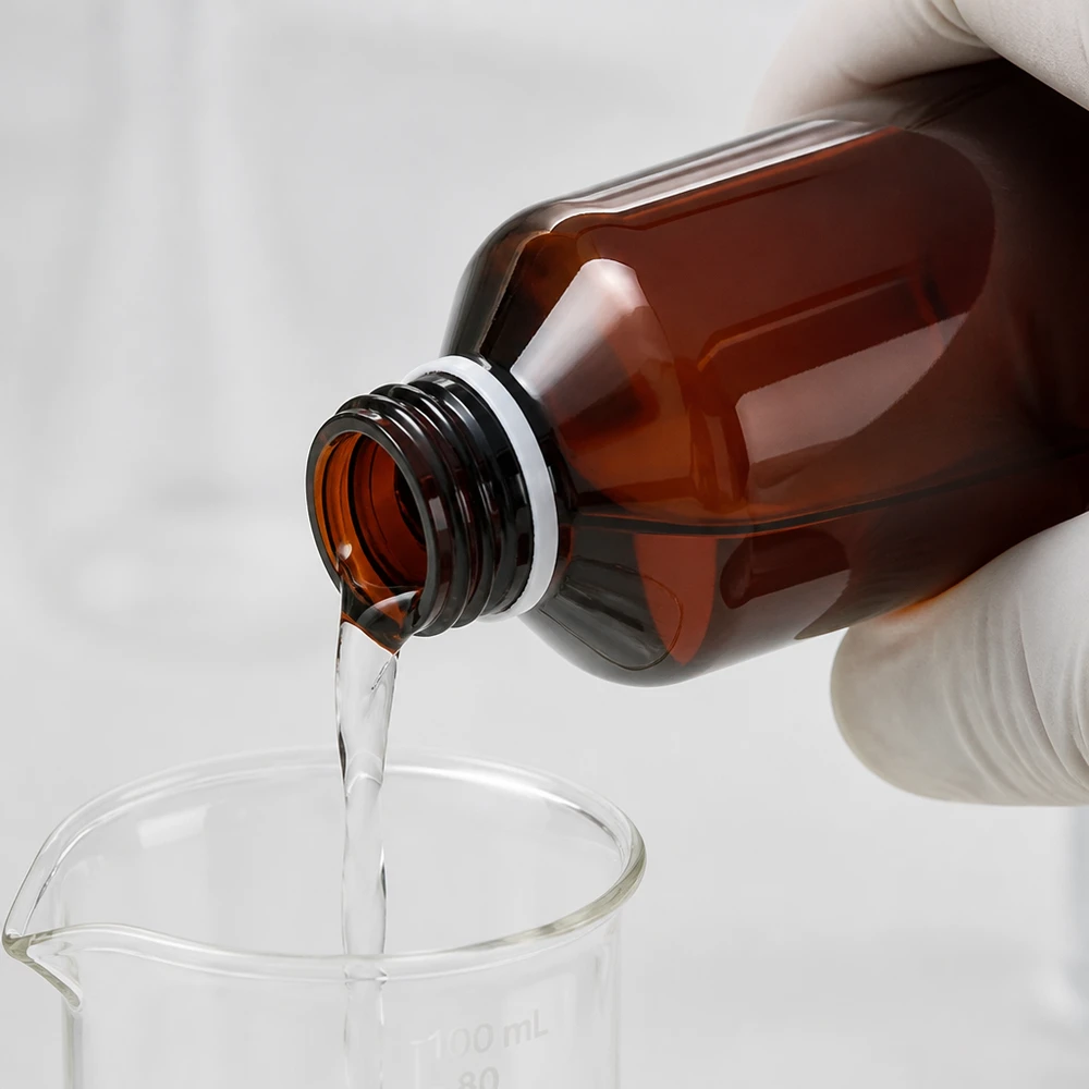 Butelka PET 200 ml z białą nakrętką typu flip-top. Czysty strumień cieczy z brązowej butelki PET o pojemności 200 ml do zlewki laboratoryjnej z rękawicą ochronną