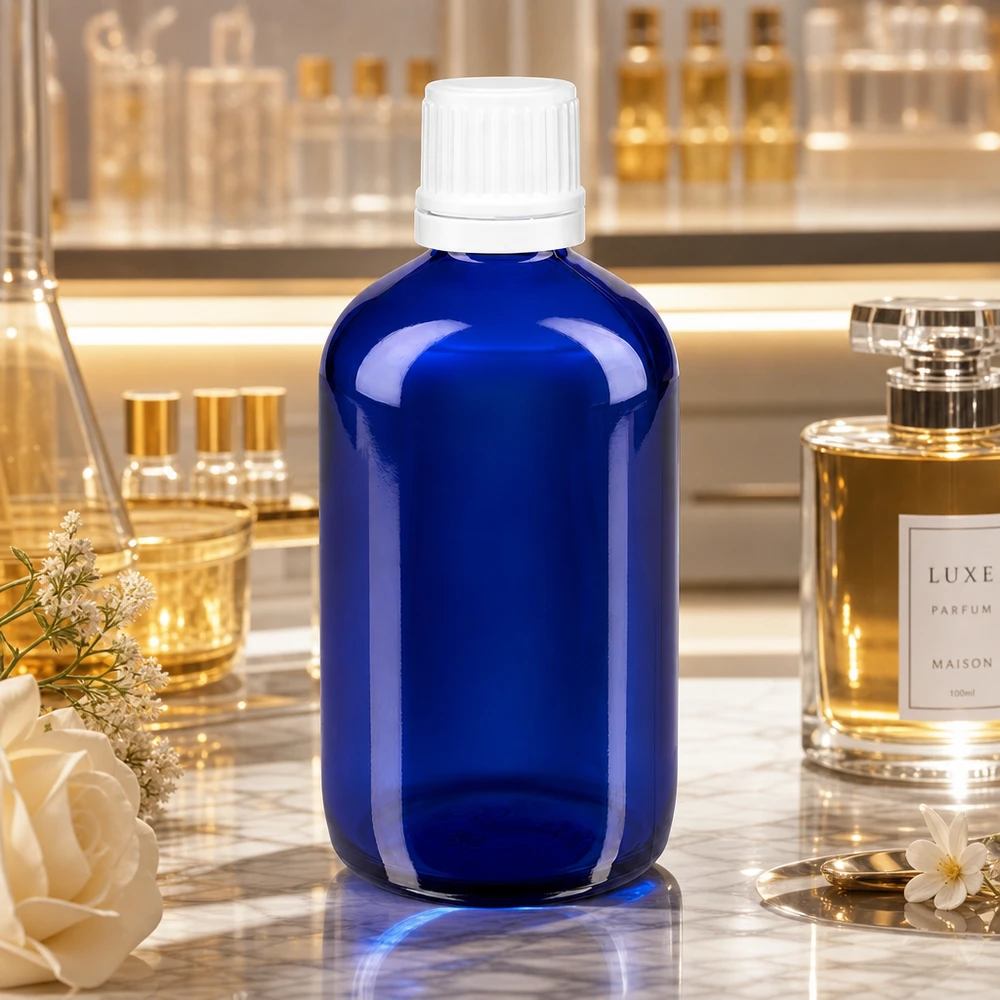 Butelka apteczna niebieska 100ml zakrętka biała OV Niebieska szklana buteleczka apteczna o pojemności 100 ml z białym zamknięciem OV 11 mm, stojąca na marmurze obok luksusowych perfum