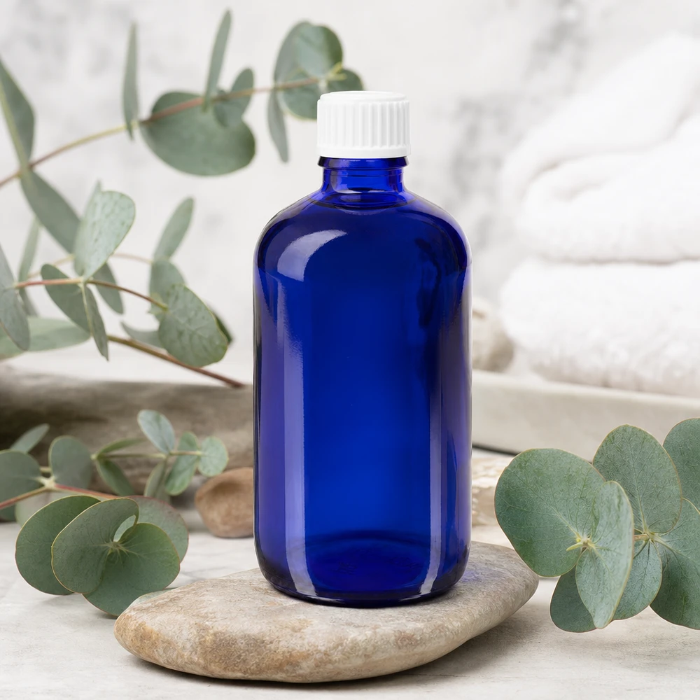 Butelka chroniąca przed światłem, 100 ml, w kolorze kobaltowym z białą zakrętką z kroplomierzem 0,9 mm, na tle kamienia naturalnego