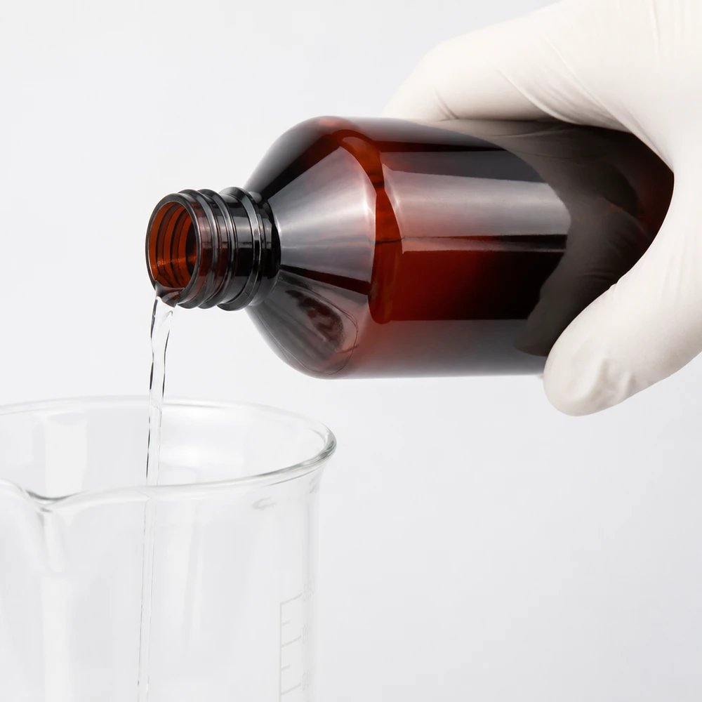 Substancję chemiczną przelewa się z brązowej butelki PET o pojemności 1 l do zlewki, mając na rękach rękawice ochronne
