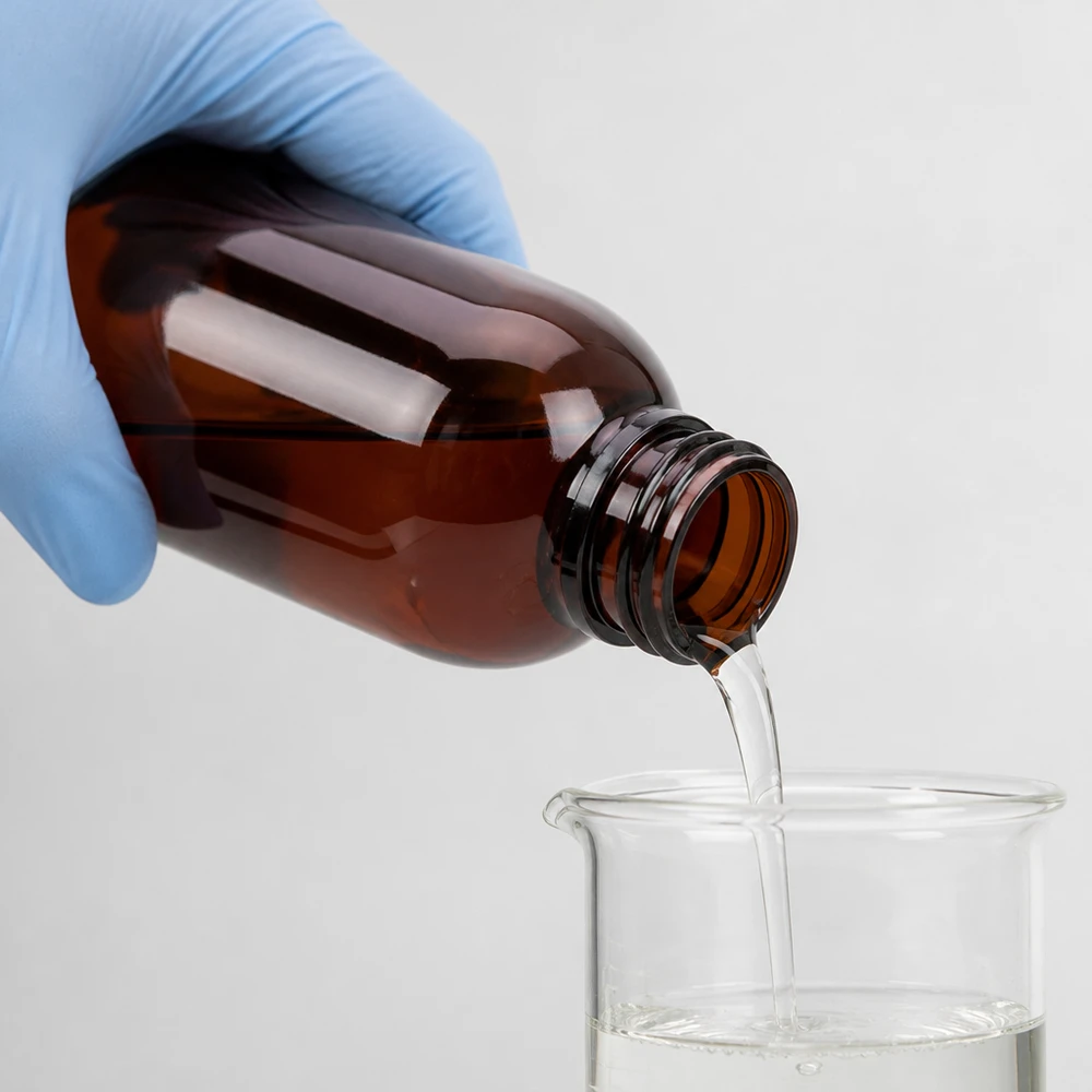 Przezroczysty płyn przelewa się z brązowej butelki PET o pojemności 250 ml do zlewki, mając na rękach rękawiczki ochronne
