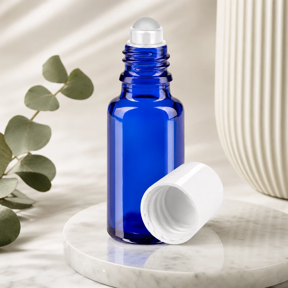 Butelka apteczna niebieska 20ml nakrętka roll-on biała Niebieska buteleczka z kulką o pojemności 20 ml, wykonana ze szkła aptecznego, z zdjętą białą nakrętką, na tle marmuru