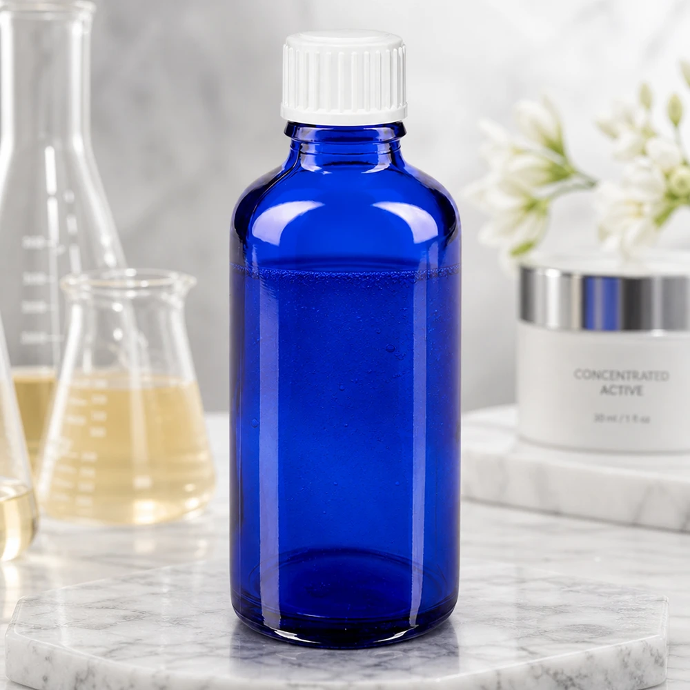 Szklana butelka o pojemności 50 ml w kolorze kobaltowym z białą zakrętką obok kolby laboratoryjnej i kremu do pielęgnacji skóry