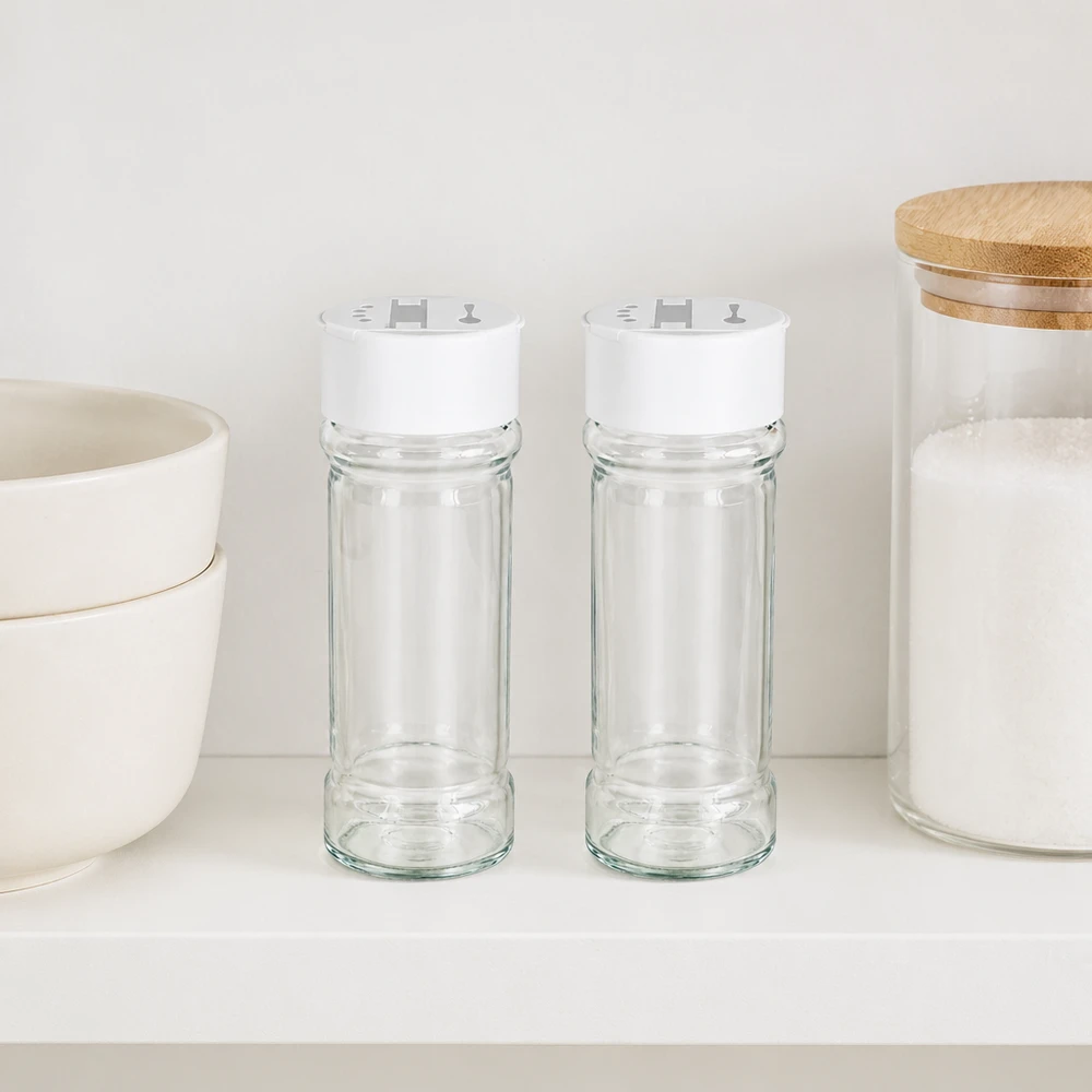 Słoik na sól/przyprawy 100 ml z podwójną dozownicą, biały Dwa słoiki na przyprawy o pojemności 100 ml z białymi pokrywkami z podwójnymi dozownikami, ustawione obok siebie na białej półce