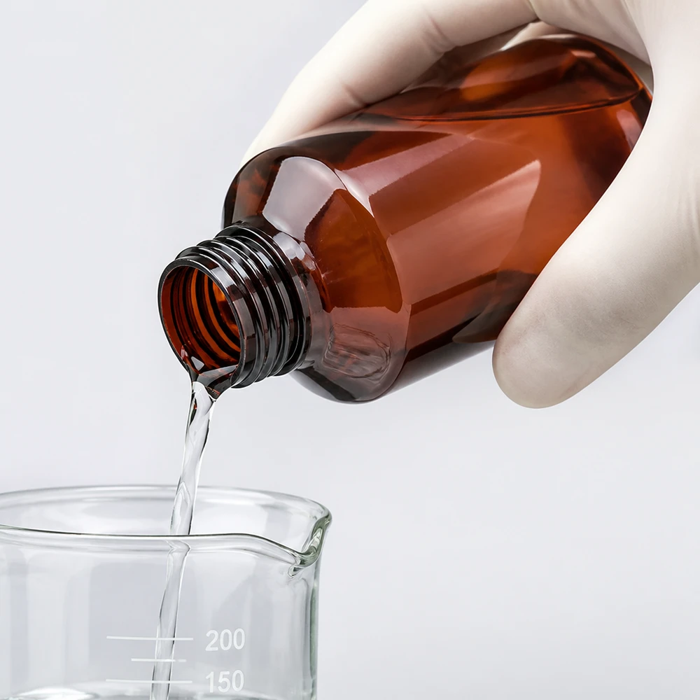 Rękawiczki podczas nalewania przezroczystego płynu z brązowej butelki PET do zlewki laboratoryjnej o pojemności 200 ml