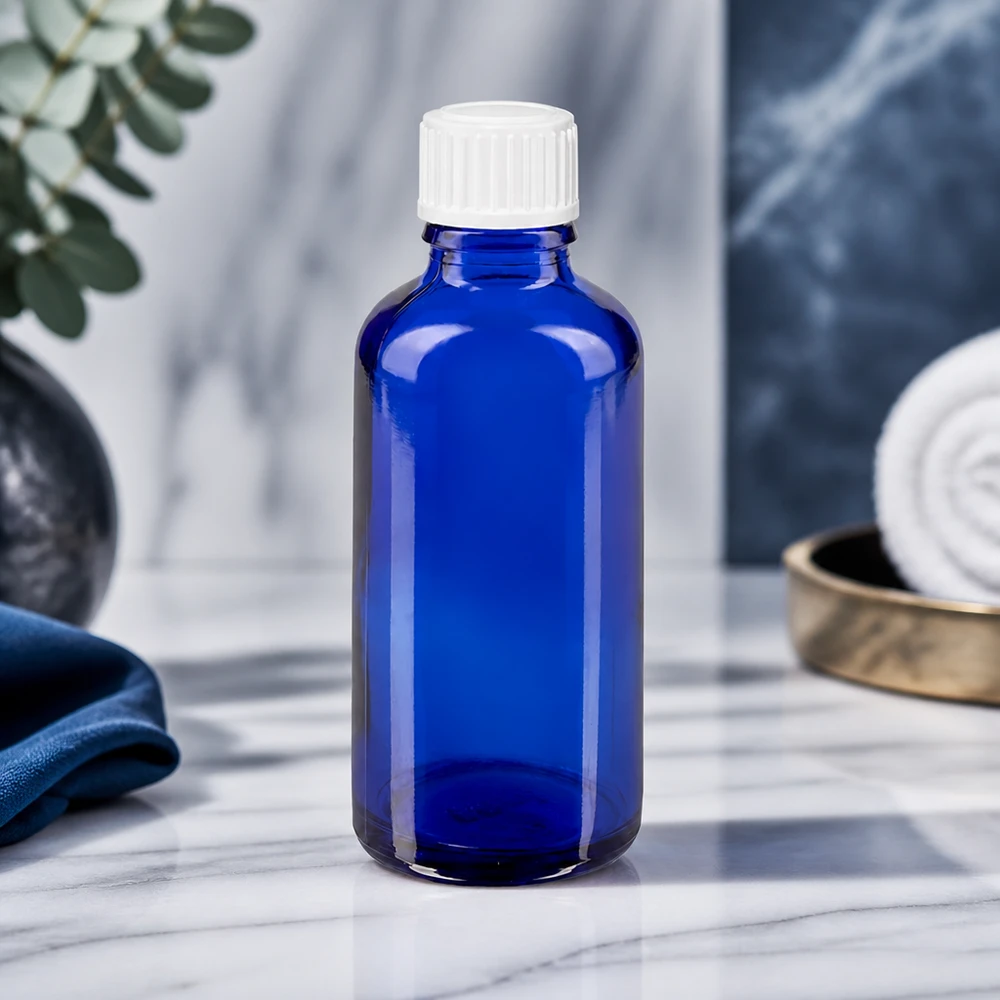 Kobaltowo-niebieska butelka z zakraplaczem STD o pojemności 50 ml, wykonana z ApoGlas, z białą nakrętką na marmurowym tle