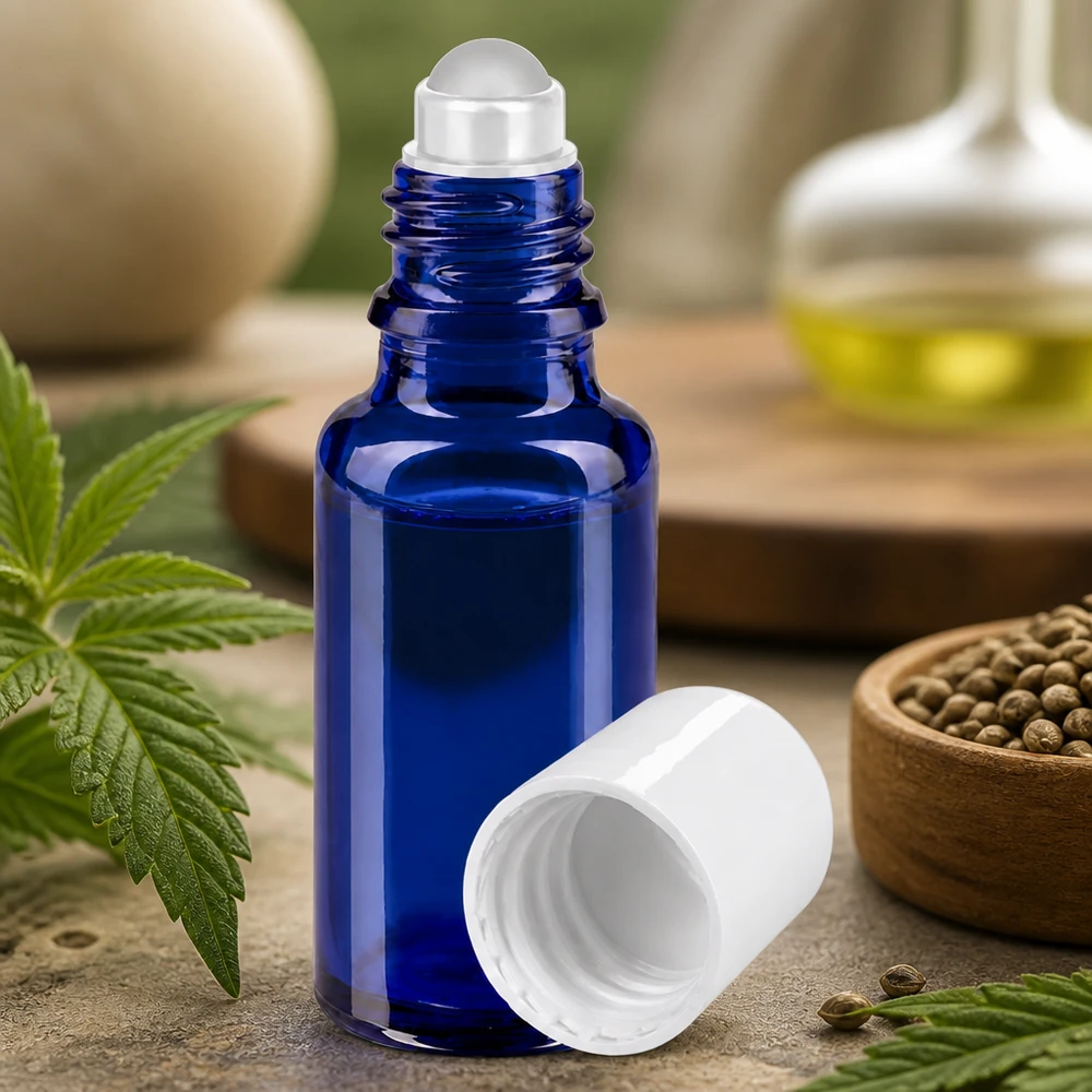 Butelka apteczna niebieska 20ml nakrętka roll-on biała Niebieska szklana buteleczka o pojemności 20 ml z kulką i białą nakrętką, otoczona liśćmi konopi i nasionami
