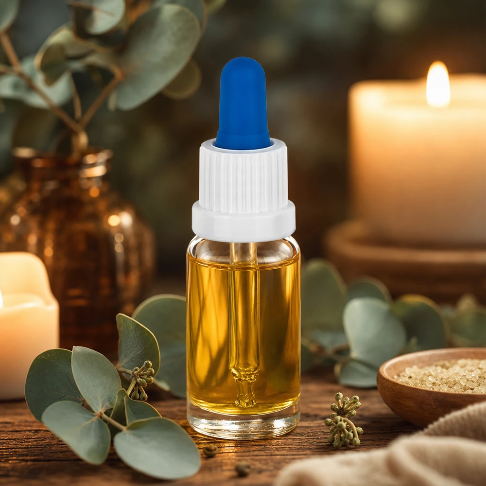 Mała buteleczka z pipetą o pojemności 10 ml, zawierająca złocisty olejek, z białą nakrętką i niebieską gumową kulką, stojąca na drewnianym stoliku