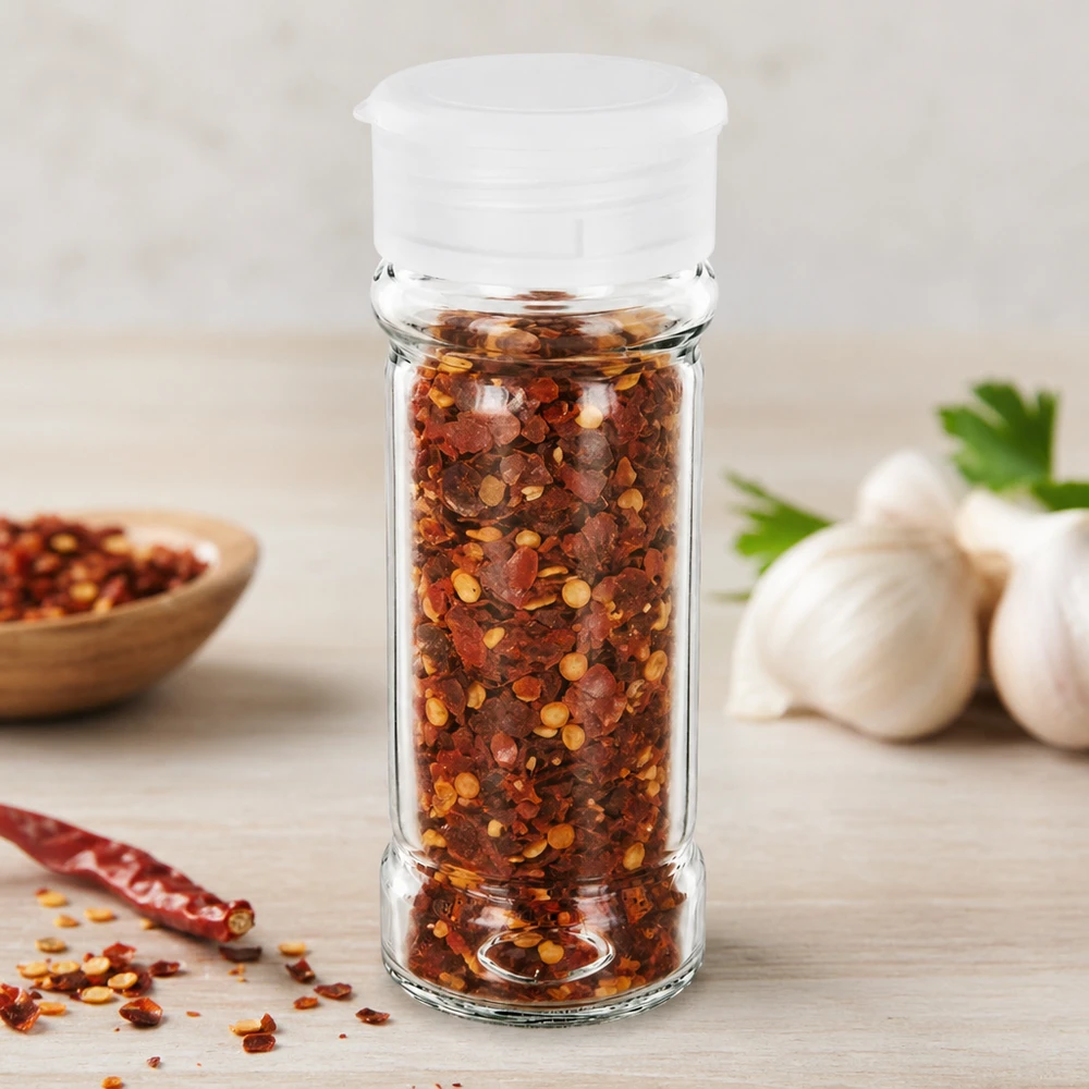 Słoik na sól/przyprawy 100 ml z dozownikiem, biały Mały słoiczek na przyprawy o pojemności 100 ml z białą posypką, wypełniony czerwonymi płatkami chili, z czosnkiem w tle