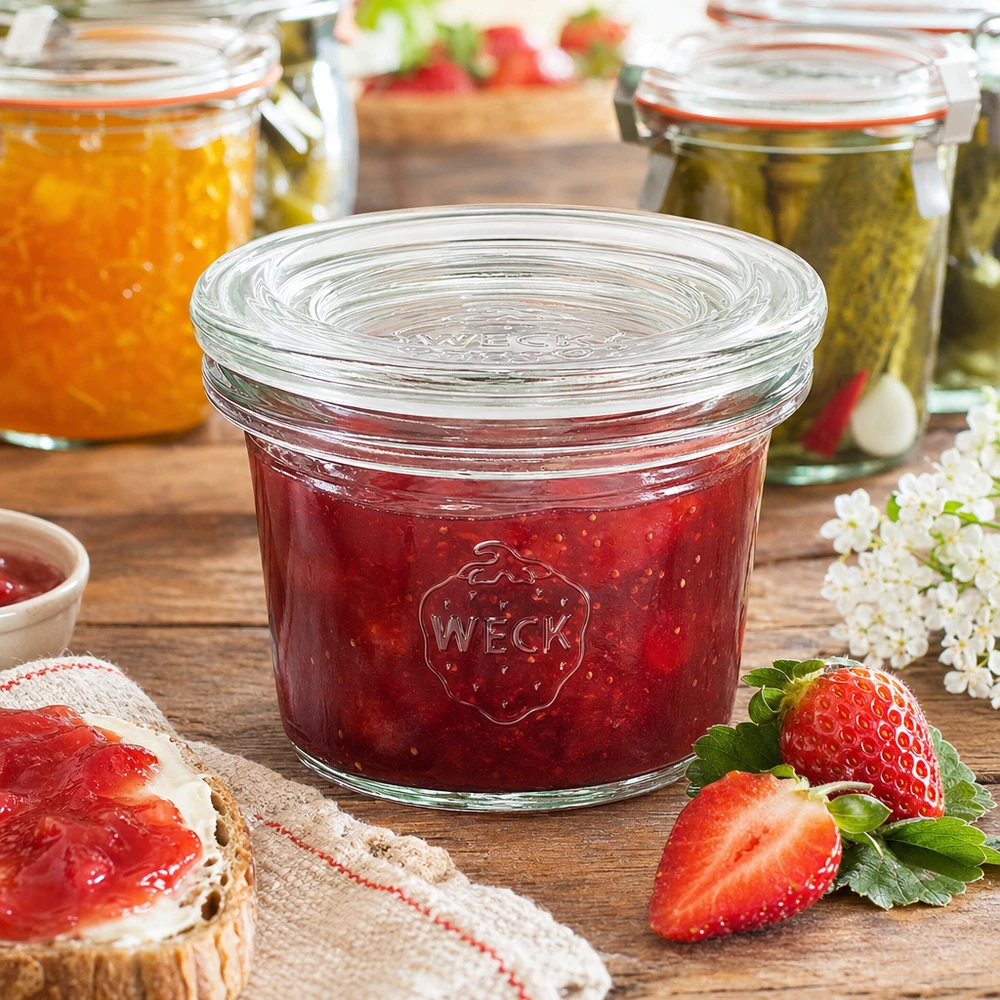 Kubki 35 ml ze szklaną pokrywką WECK RR40 Słoik WECK 35ml RR40 wypełniony dżemem z czerwonych truskawek obok świeżych truskawek i chleba z dżemem