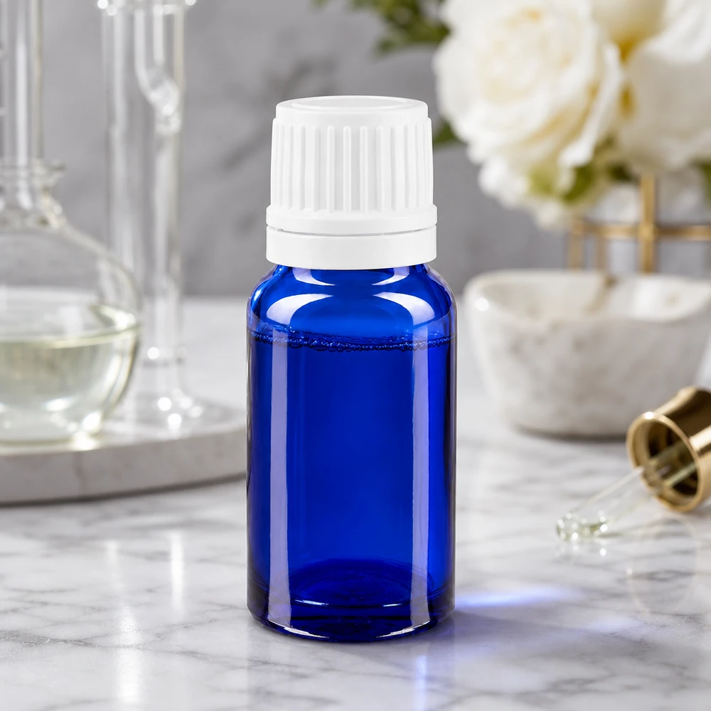 Butelka apteczna niebieska 10ml drip v. 1,2 mm biały OV Butelka apteczna o pojemności 10 ml z niebieskiego szkła z białym zakraplaczem, stojąca na marmurowej powierzchni obok róż