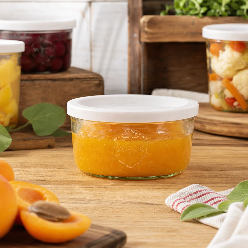 Kubki o pojemności 165 ml z pokrywką WECK RR80 Słoik WECK 165 ml wypełniony dżemem pomarańczowym w naturalnym otoczeniu kuchni ze słoikami na przetwory w tle