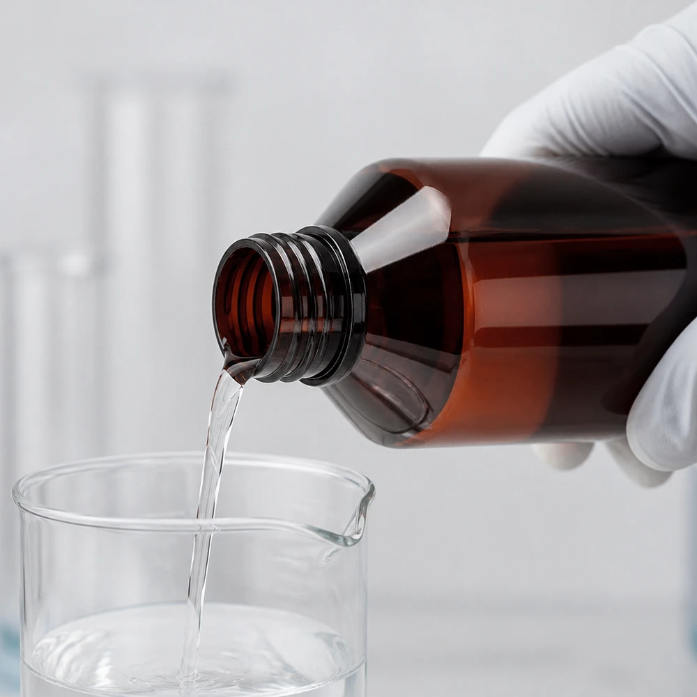 Butelka PET 750 ml z zieloną nakrętką OV Laborant w białych rękawiczkach przelewa przezroczysty płyn z brązowej butelki PET o pojemności 750 ml do zlewki