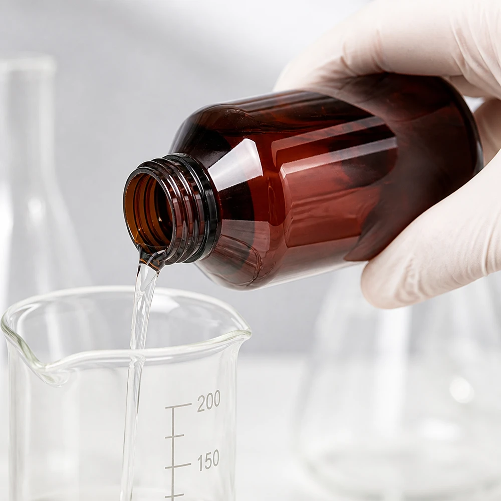 Przezroczysty płyn przelewa się z brązowej butelki PET o pojemności 100 ml do szklanej zlewki