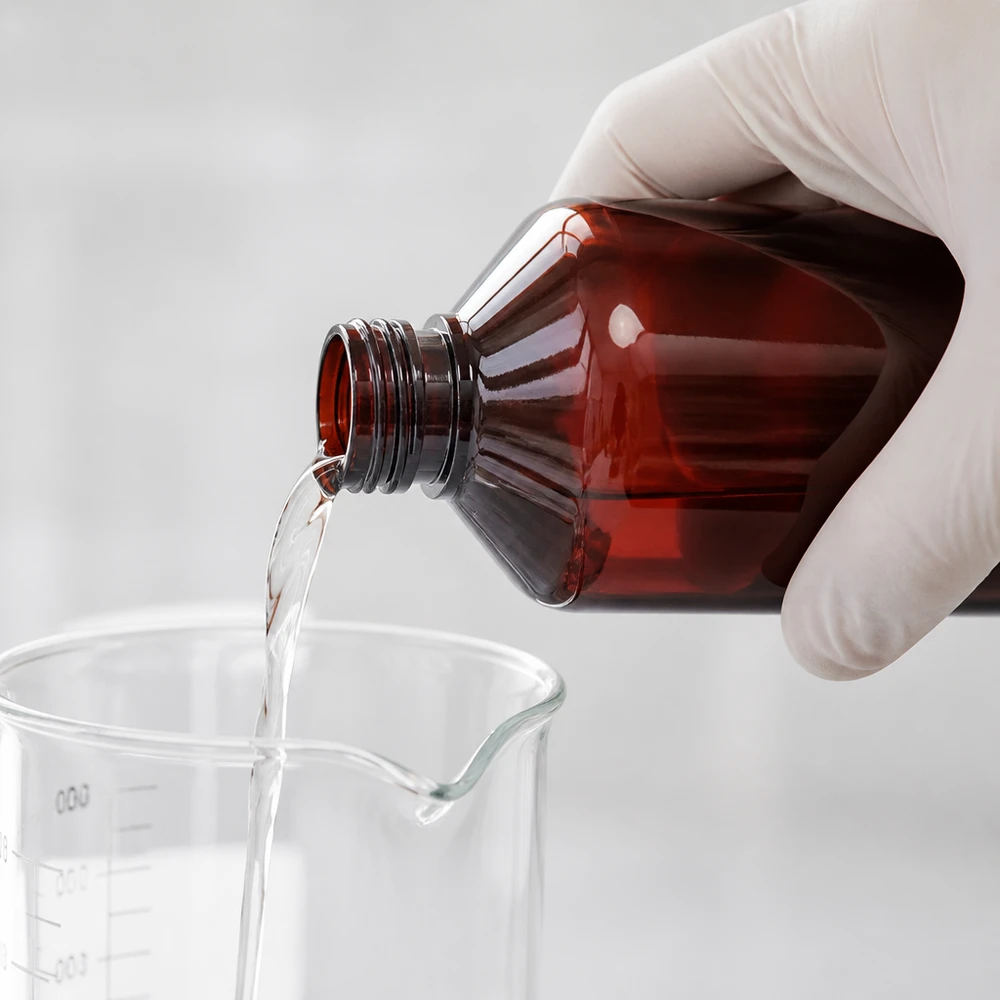 Butelka PET 500ml PP28 bez zakrętki Laborant w białej rękawiczce wlewa przezroczysty płyn z brązowej butelki PET o pojemności 500 ml do zlewki