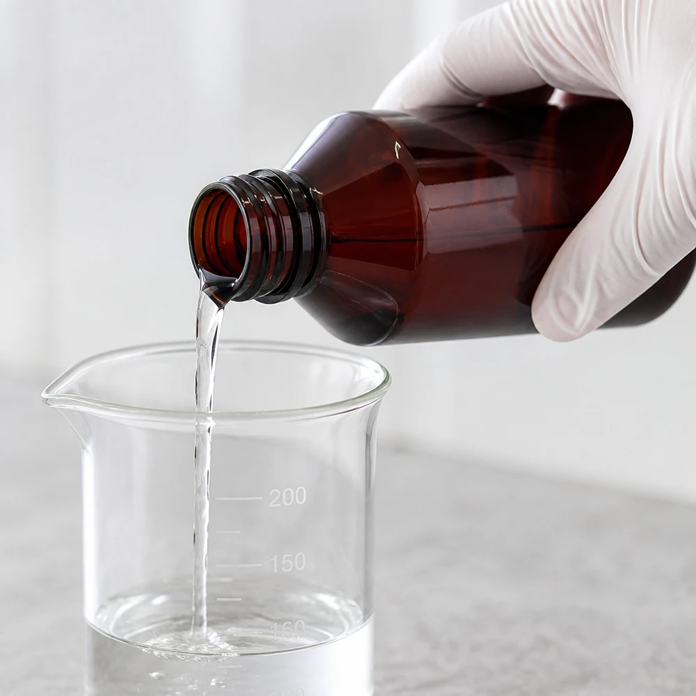 Butelka PET 750 ml z atomizerem biała Osoba z okularami przelewa przezroczysty płyn z brązowej butelki PET o pojemności 750 ml do szklanej zlewki