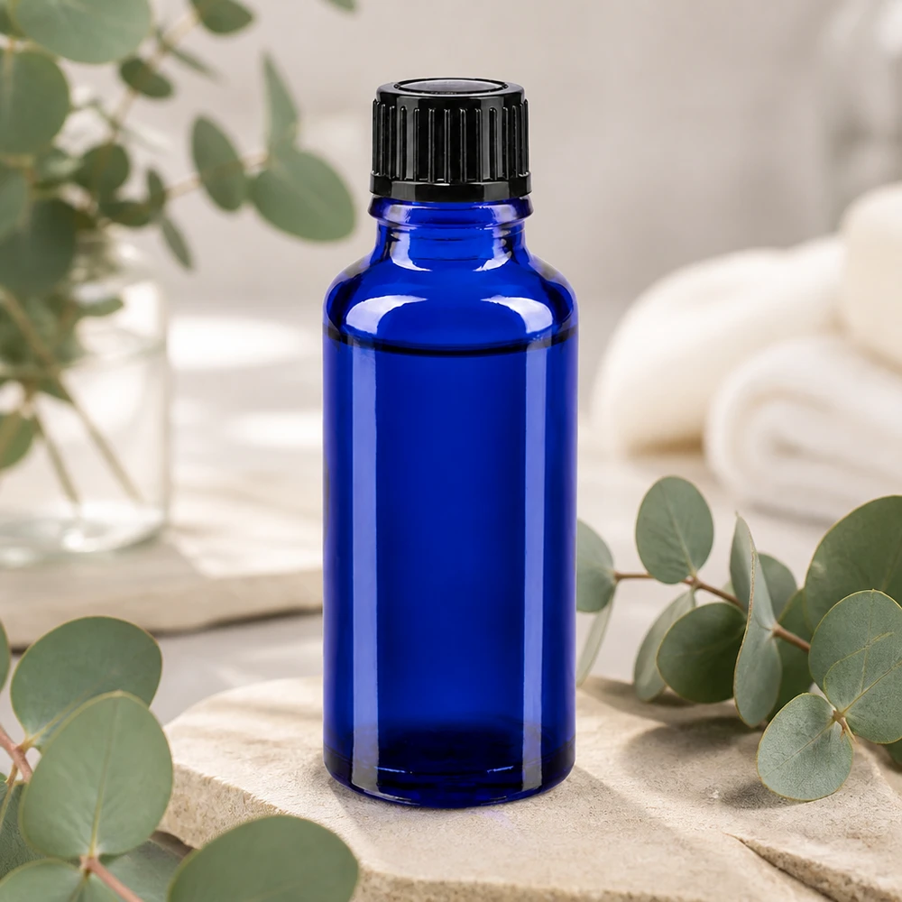 Szklana buteleczka o pojemności 30 ml w kolorze kobaltowym z czarną nakrętką dozującą, umieszczona na kamieniu naturalnym z gałązkami eukaliptusa