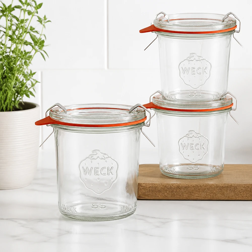 Trzy kubki WECK 140 ml RR60 ułożone na drewnianej desce w nowoczesnej kuchni z zieloną rośliną w tle