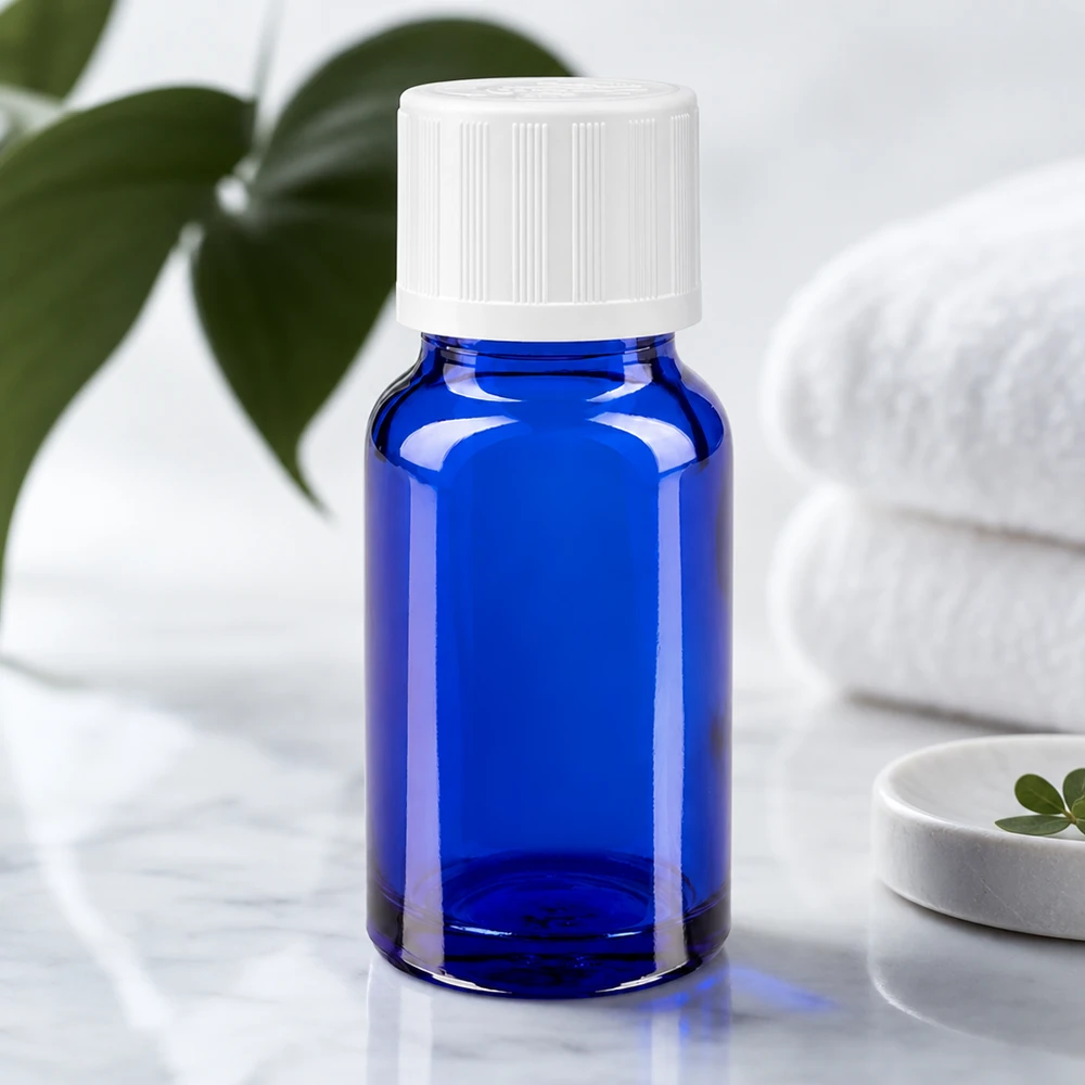 Butelka apteczna niebieska 10ml z kroplomierzem biała KiSi St 10 ml niebieska szklana buteleczka apteczna z białą nakrętką zabezpieczającą przed dziećmi, stojąca na marmurze obok złożonych ręczników