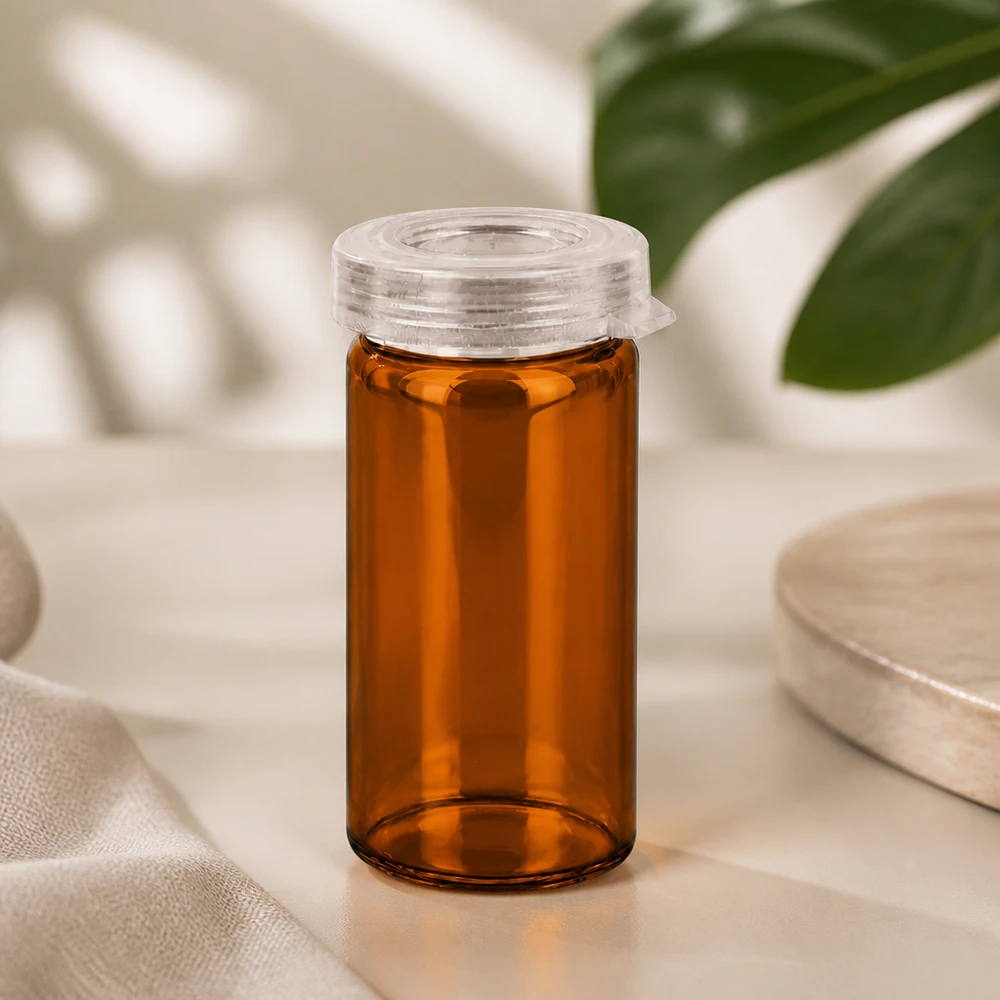 Szklana tubka na tabletki w kolorze bursztynowym o pojemności 5 ml z przezroczystą plastikową pokrywką zatrzaskową na jasnym tle