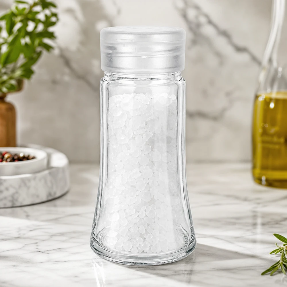 Sólnik szklany o pojemności 95 ml, wypełniony gruboziarnistą solą morską, na białym marmurowym blacie