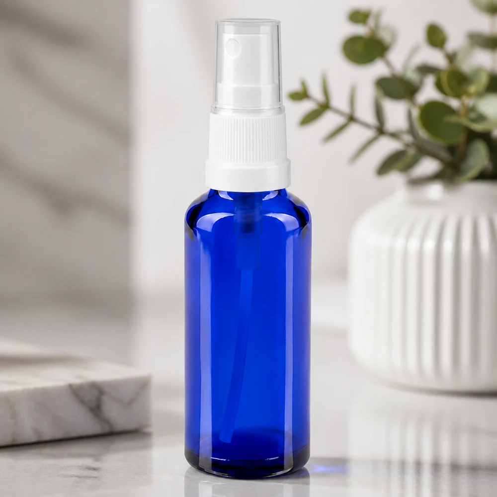 Butelka apteczna niebieska 30ml spray top biały Niebieska szklana buteleczka apteczna o pojemności 30 ml z białą głowicą rozpylającą na tle białego marmuru